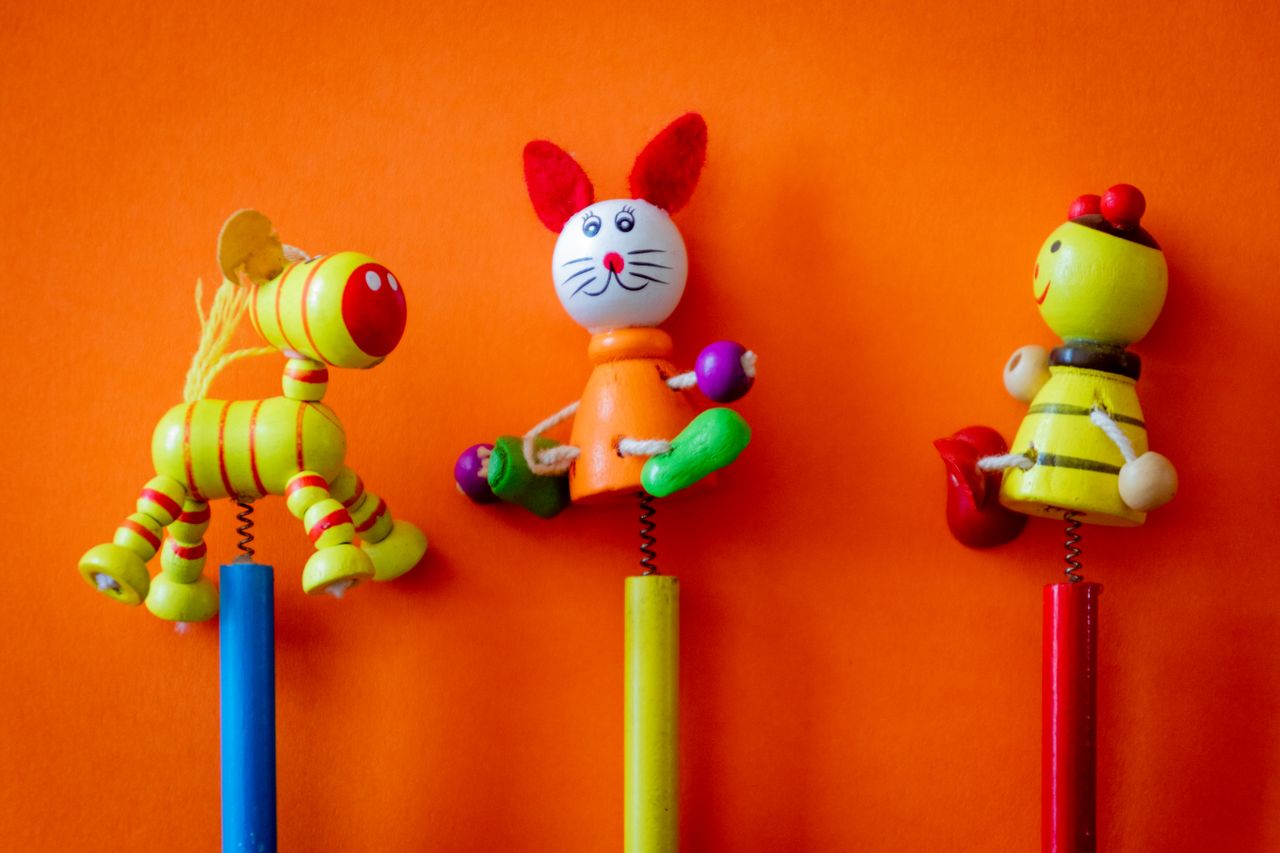 services-01 Close-up of three colorful wooden toys on a vibrant orange background, perfect for children's themes.