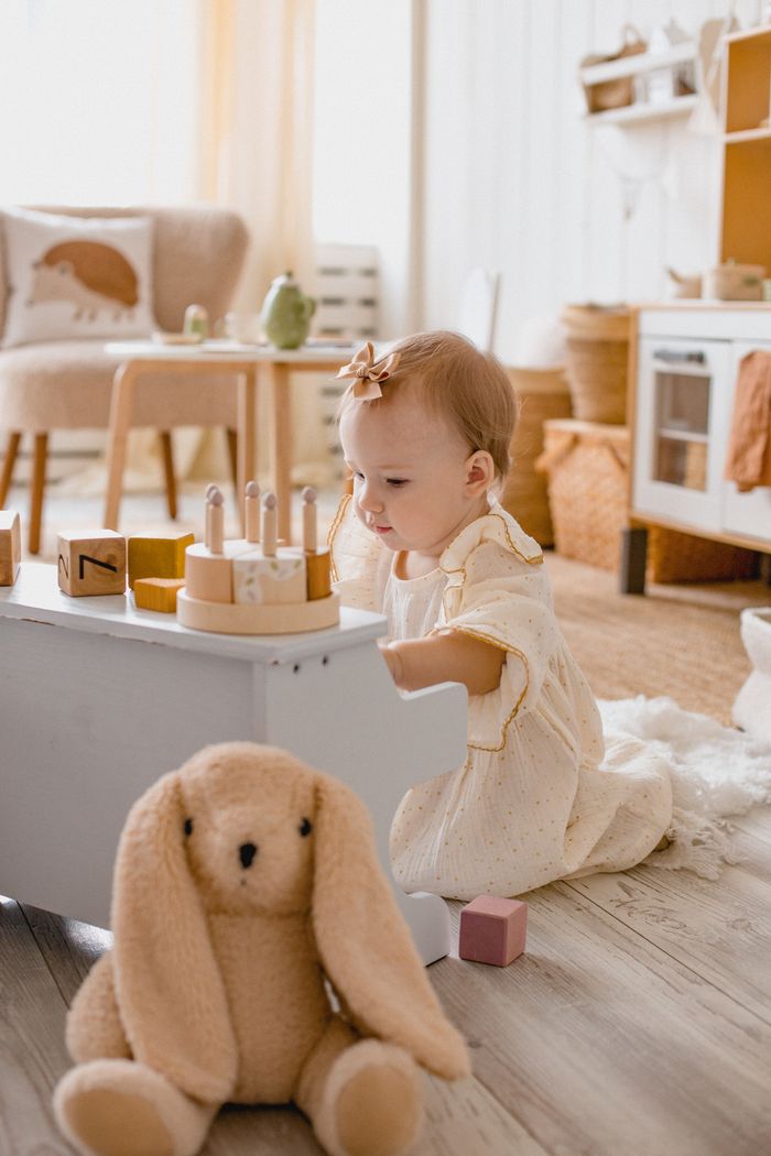 services-02 A cute toddler playing joyfully in a stylish and cozy nursery setting with soft toys and wooden blocks.