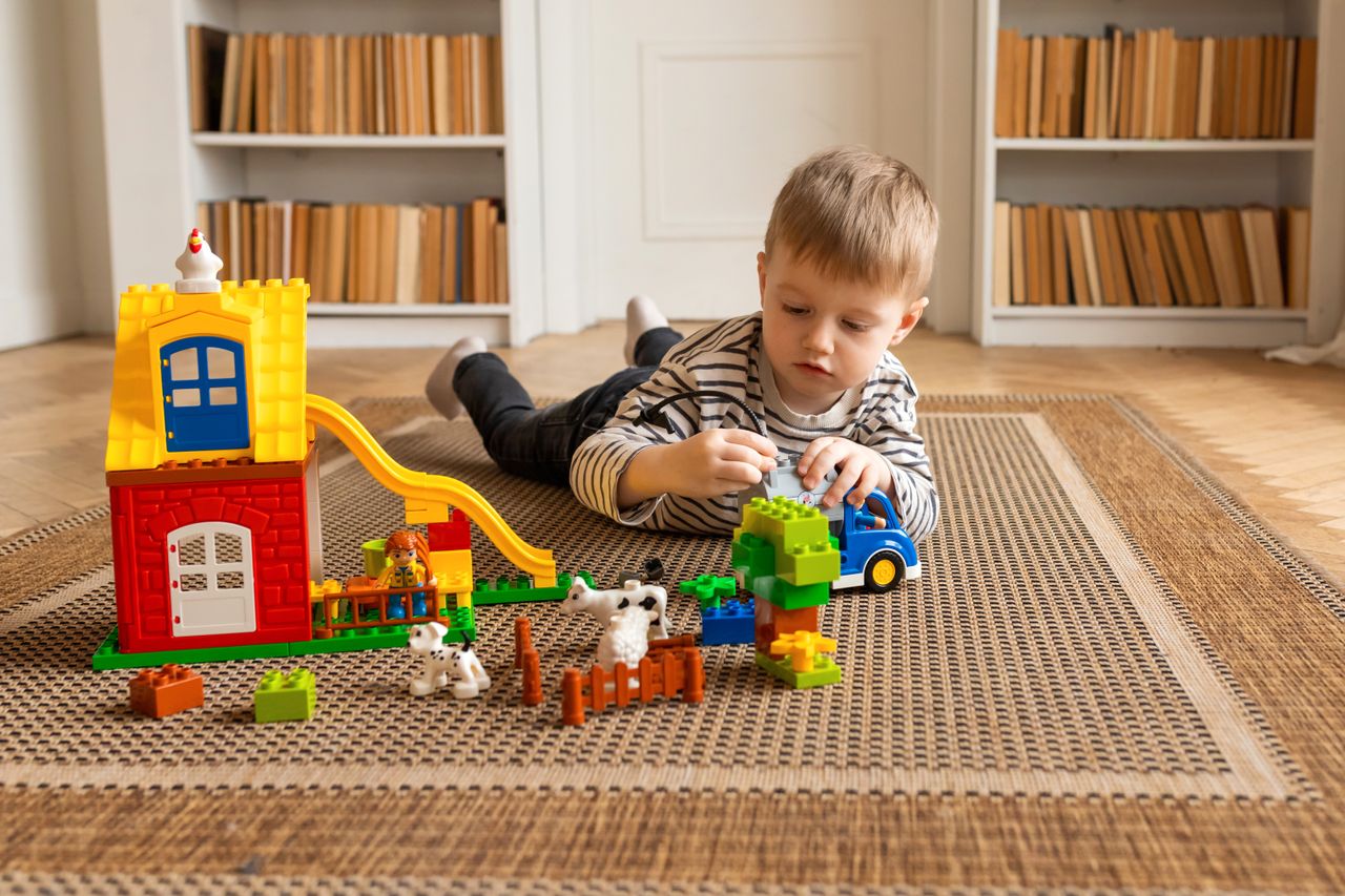 team-02 Young boy engaged in imaginative block play on a carpeted floor indoors.
