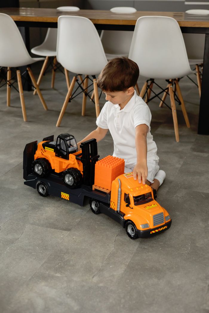 services-03 A young boy playing with a toy truck set on a smooth indoor floor.