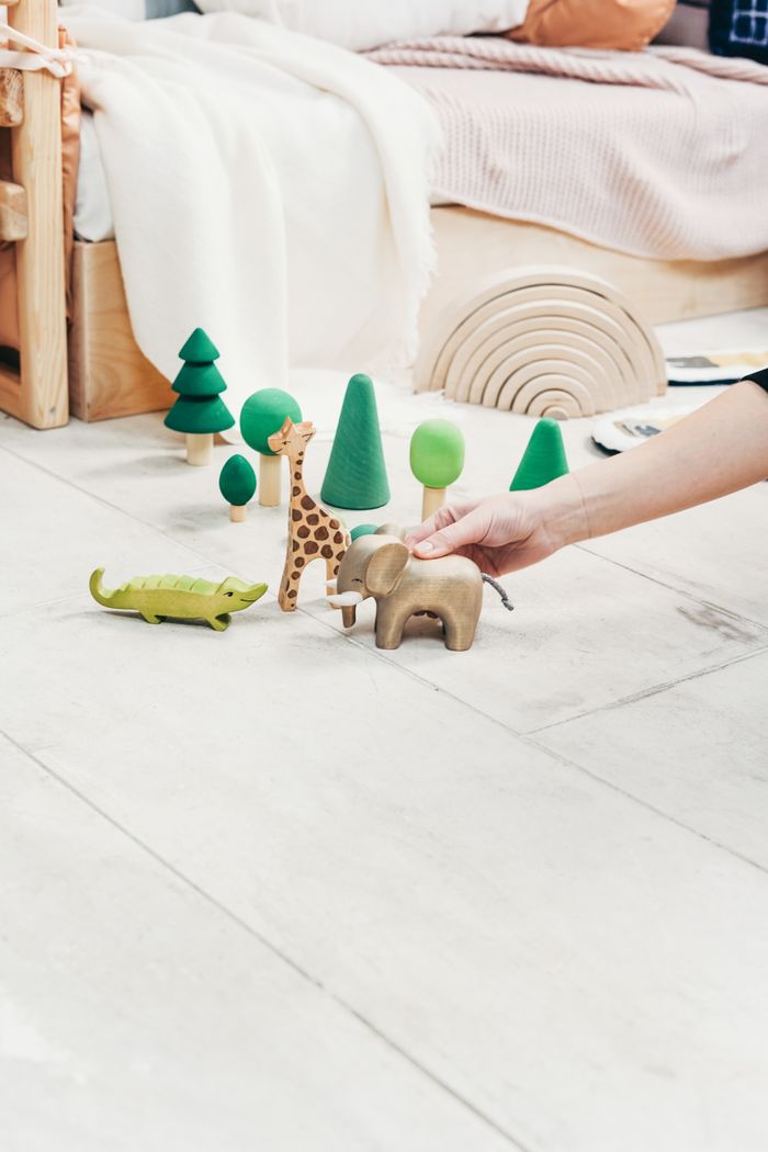 who-we-are A playful indoor scene featuring a child's hand engaging with wooden toy animals and trees.