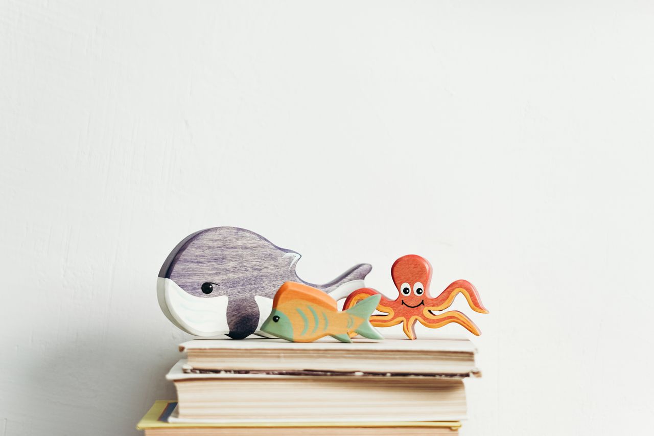 services-04 Charming wooden toys of marine animals on stacked books with a white background, perfect for kids' decor.