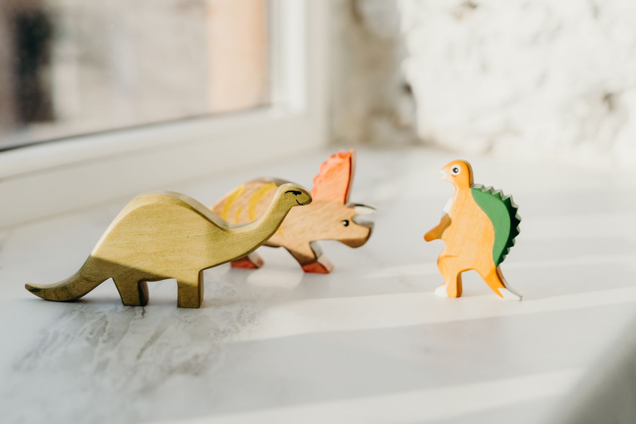 why-choose-us A delightful set of wooden dinosaur toys basking in natural light by the window, capturing playful innocence.